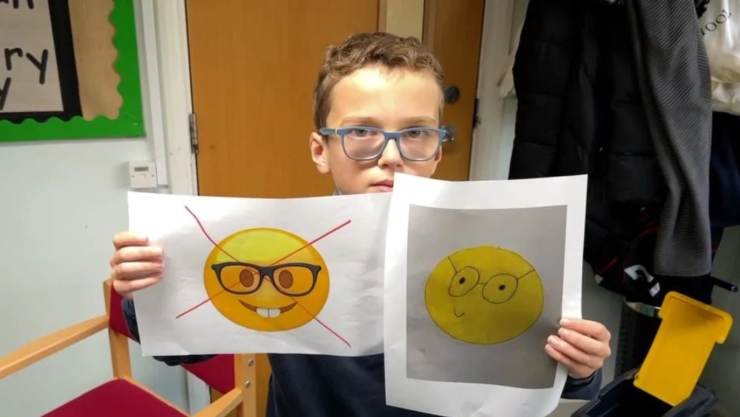 Teddy holds up the current offending nerd face emoji with his own replacement genius emoji on the right. Image credit BBC - 10-year-old Teddy starts petition to get Apple to change offensive emoji